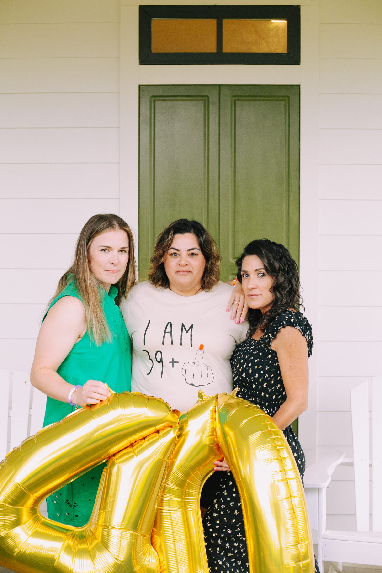 Three friends celebrating a birthday with gold balloons
