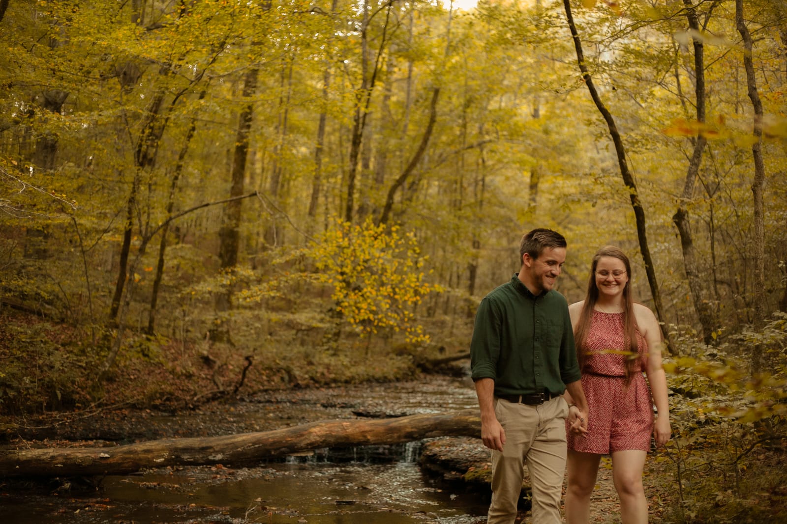 Couple walking through autumn woods by stream