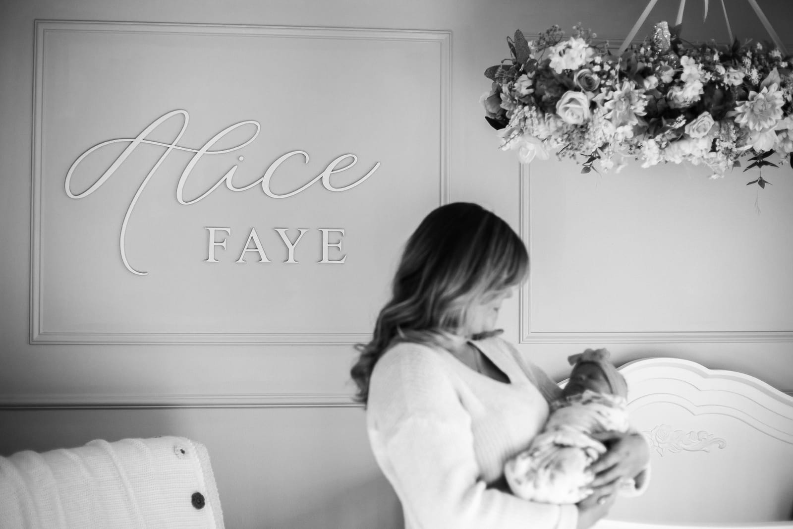 Mother holding baby in nursery with name sign