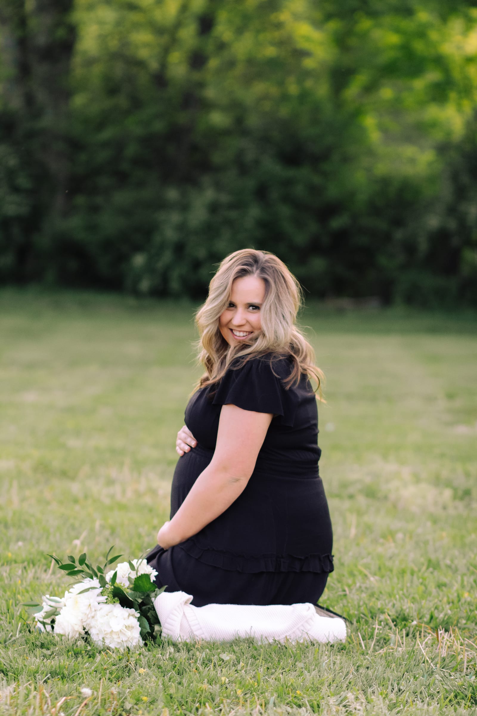 Expecting mother kneeling in a field beside white flowers